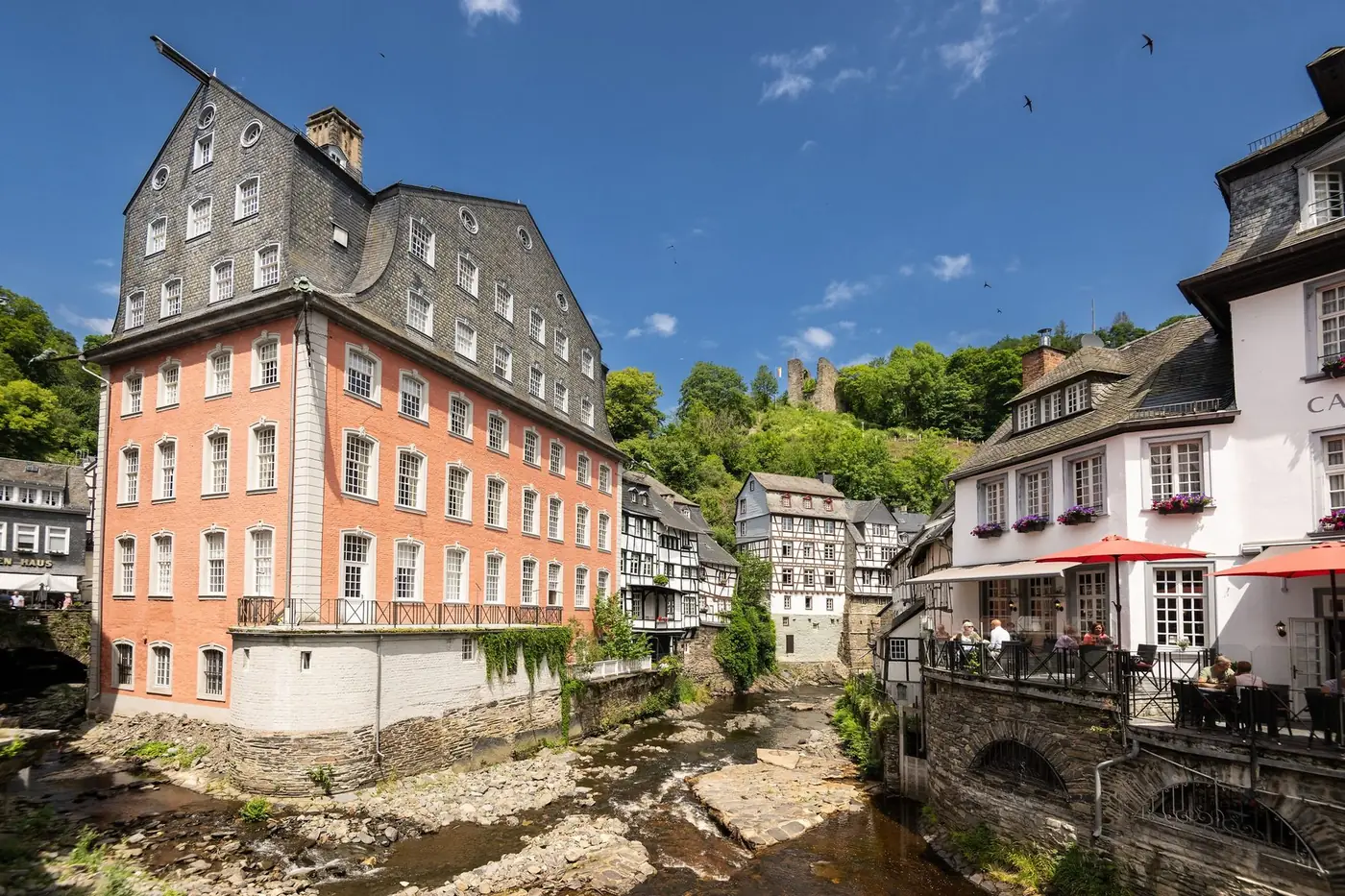 Het Rode Huis en vakwerkhuizen aan de Rur in Monschau, met daarboven de burchtruïne op de helling
